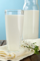 Photo of Fresh milk and blossoms on wooden table against light blue background, closeup