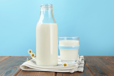 Photo of Fresh milk and flowers on wooden table against light blue background, closeup