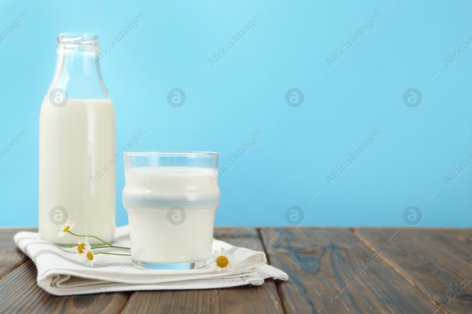 Fresh milk and flowers on wooden table against light blue background, closeup. Space for text Photo of Fresh milk and flowers on wooden table against light blue background, closeup. Space for text