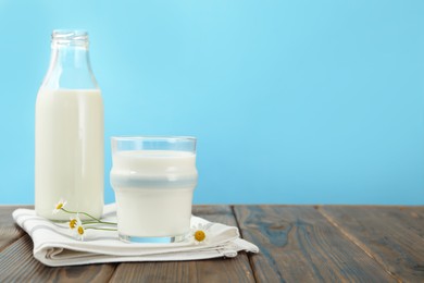 Photo of Fresh milk and flowers on wooden table against light blue background, closeup. Space for text