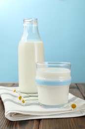 Photo of Fresh milk and flowers on wooden table against light blue background, closeup