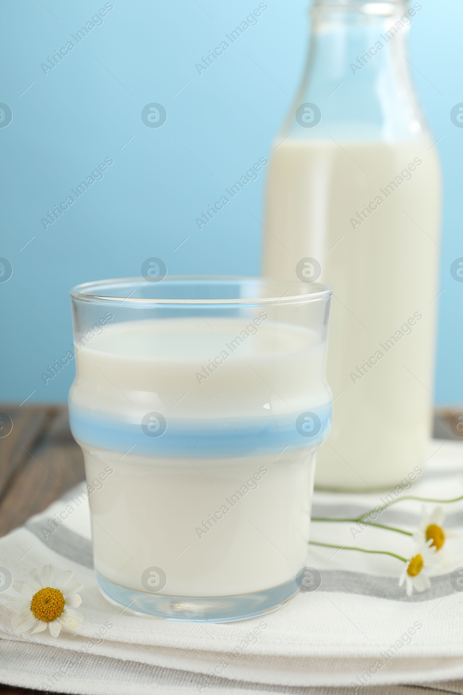 Fresh milk and flowers on wooden table against light blue background, closeup Photo of Fresh milk and flowers on wooden table against light blue background, closeup