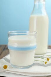 Photo of Fresh milk and flowers on wooden table against light blue background, closeup