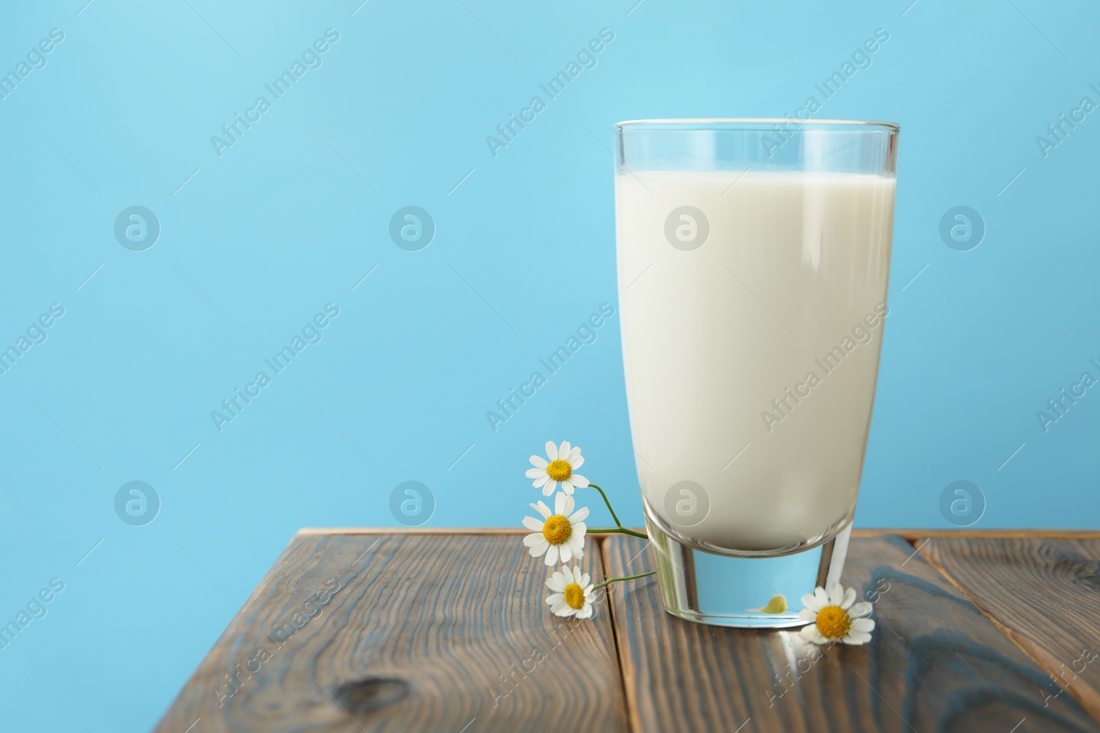 Fresh milk in glass and flowers on wooden table against light blue background, closeup. Space for text Photo of Fresh milk in glass and flowers on wooden table against light blue background, closeup. Space for text