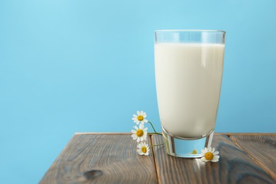 Photo of Fresh milk in glass and flowers on wooden table against light blue background, closeup. Space for text