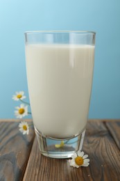 Photo of Fresh milk in glass and flowers on wooden table against light blue background, closeup