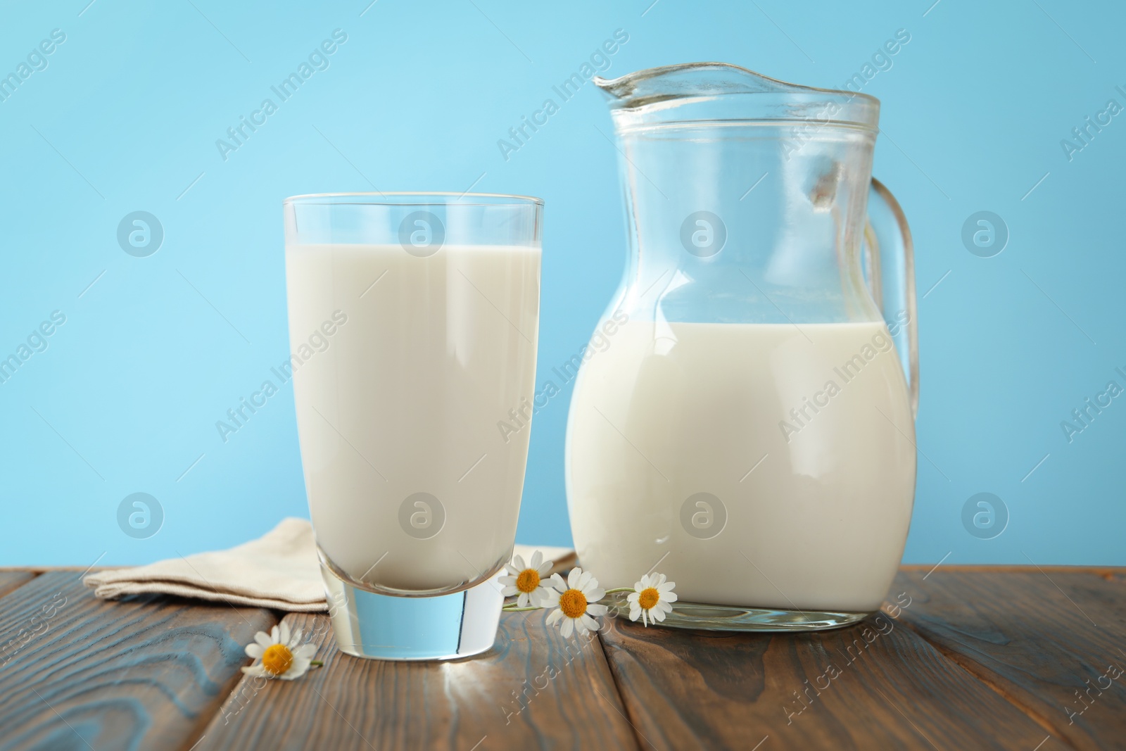 Fresh milk and flowers on wooden table against light blue background, closeup Photo of Fresh milk and flowers on wooden table against light blue background, closeup