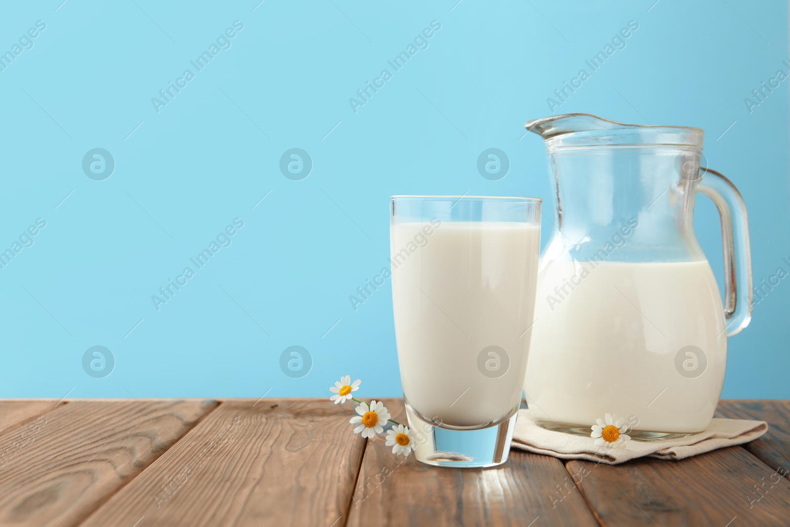 Fresh milk and flowers on wooden table against light blue background, closeup. Space for text Photo of Fresh milk and flowers on wooden table against light blue background, closeup. Space for text