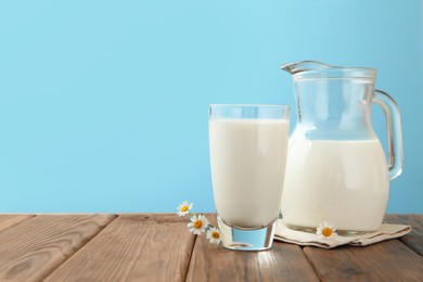 Photo of Fresh milk and flowers on wooden table against light blue background, closeup. Space for text