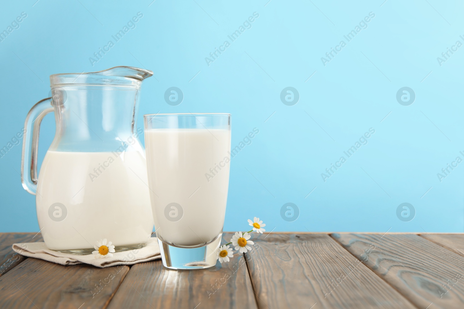 Fresh milk and flowers on wooden table against light blue background, closeup. Space for text Photo of Fresh milk and flowers on wooden table against light blue background, closeup. Space for text