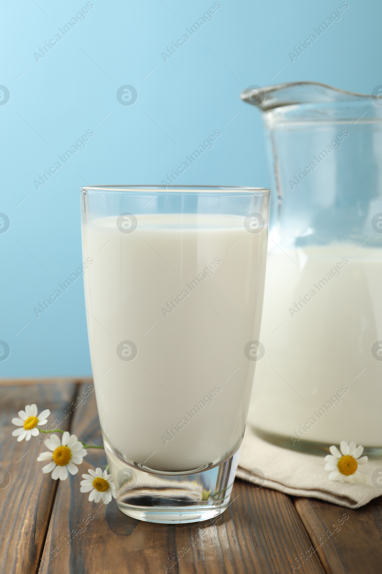 Fresh milk and flowers on wooden table against light blue background, closeup Photo of Fresh milk and flowers on wooden table against light blue background, closeup