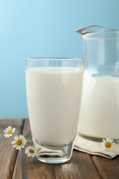 Photo of Fresh milk and flowers on wooden table against light blue background, closeup