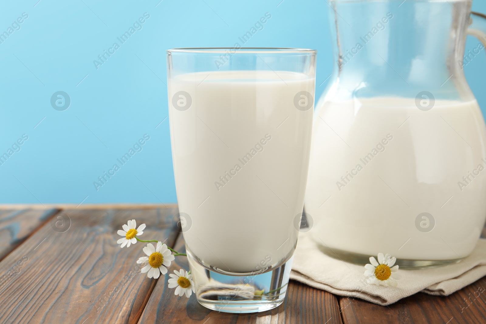 Fresh milk and flowers on wooden table against light blue background, closeup Photo of Fresh milk and flowers on wooden table against light blue background, closeup