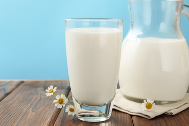 Photo of Fresh milk and flowers on wooden table against light blue background, closeup