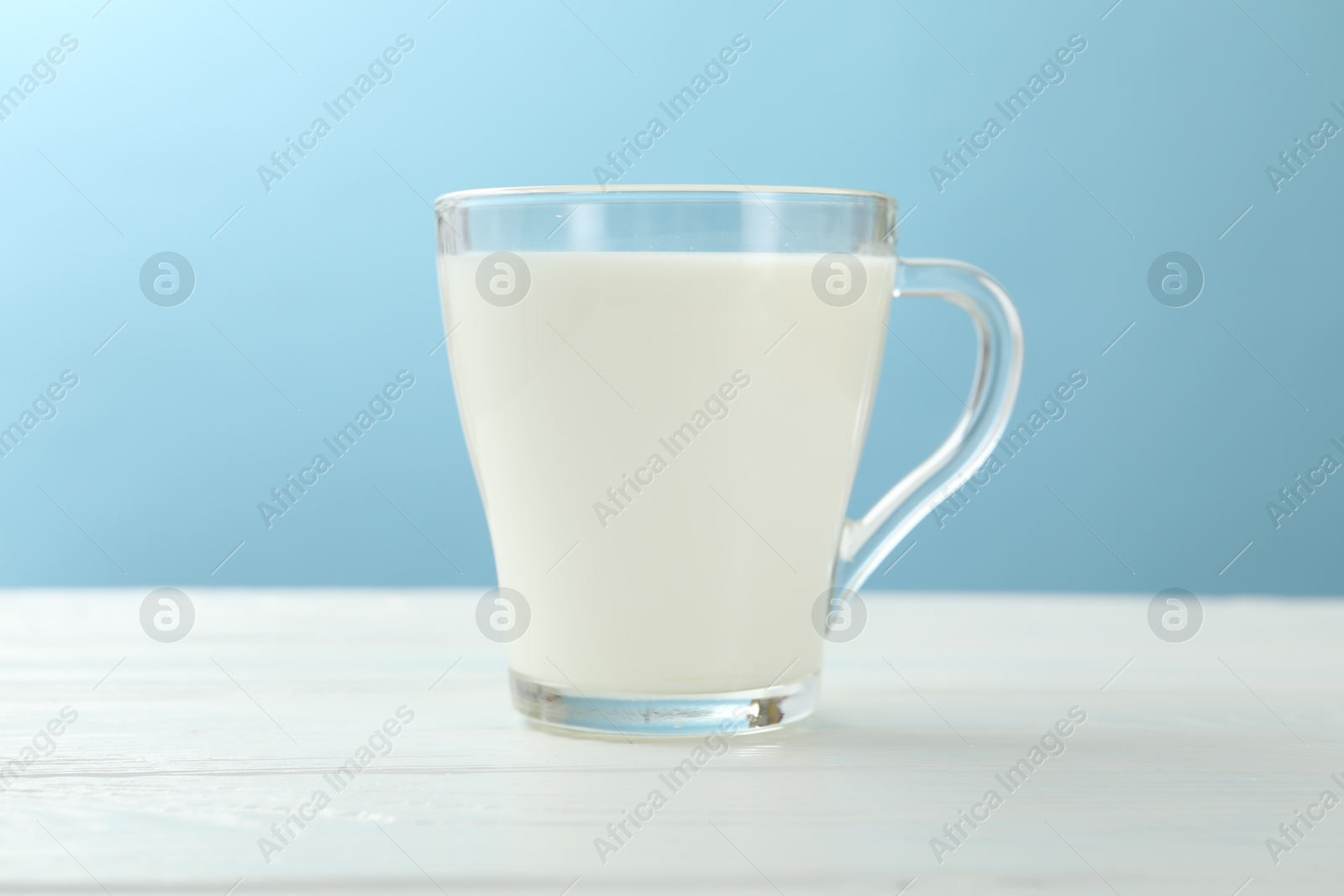 Fresh milk in glass cup on white wooden table against light blue background, closeup Photo of Fresh milk in glass cup on white wooden table against light blue background, closeup
