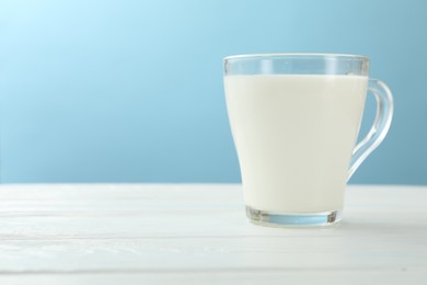 Photo of Fresh milk in glass cup on white wooden table against light blue background, closeup