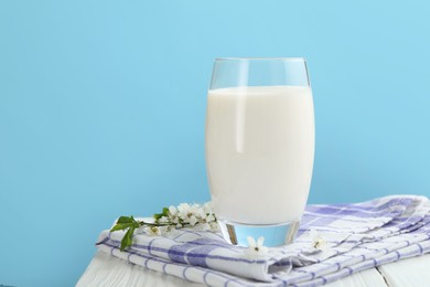 Photo of Fresh milk in glass and blossoms on white wooden table against light blue background, closeup