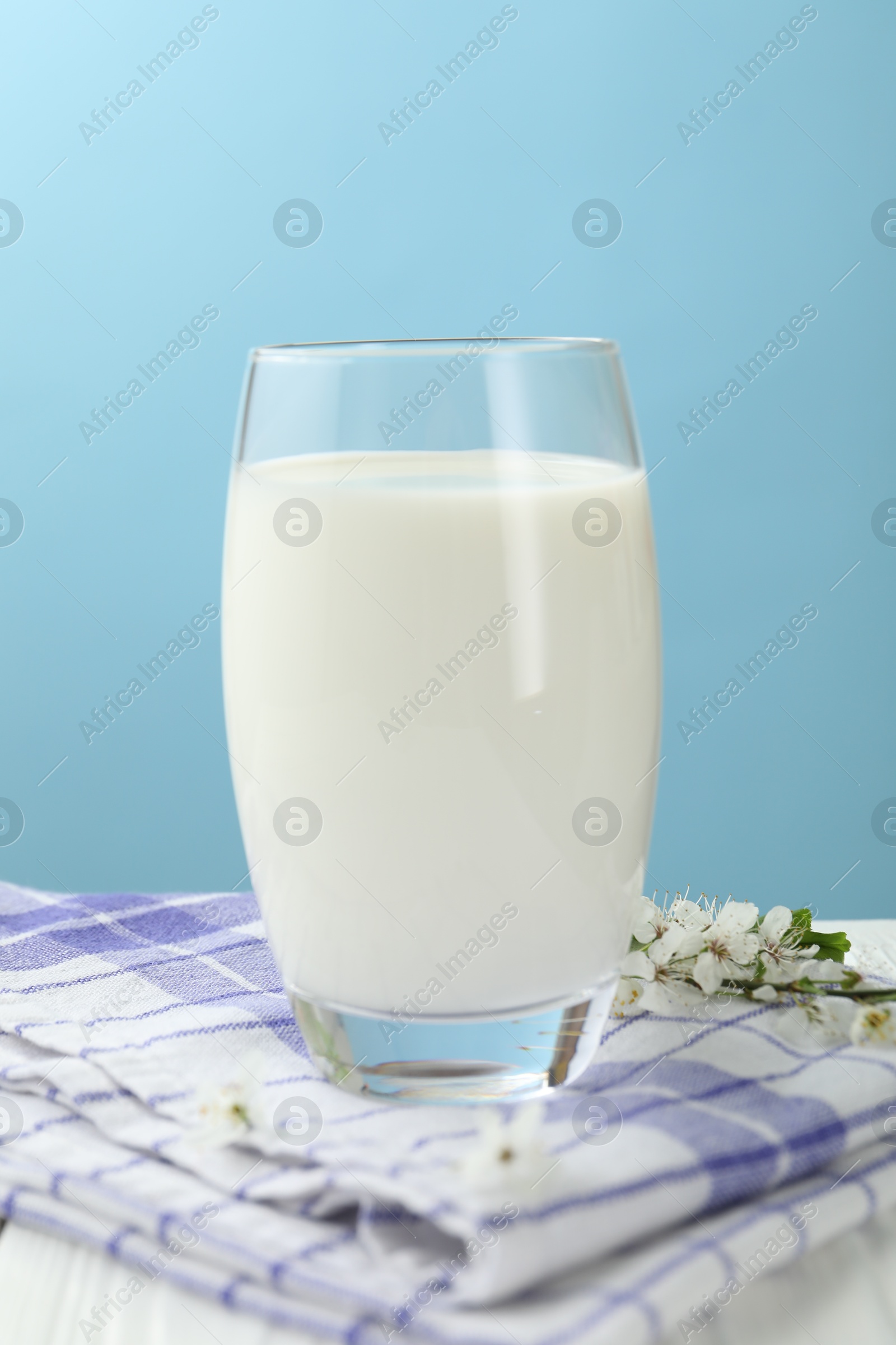 Fresh milk in glass and blossoms on white wooden table against light blue background, closeup Photo of Fresh milk in glass and blossoms on white wooden table against light blue background, closeup