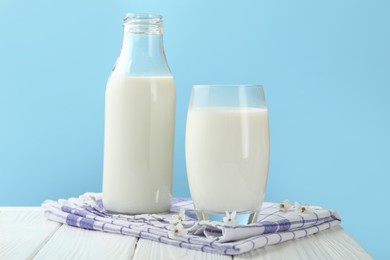 Photo of Fresh milk and blossoms on white wooden table against light blue background, closeup