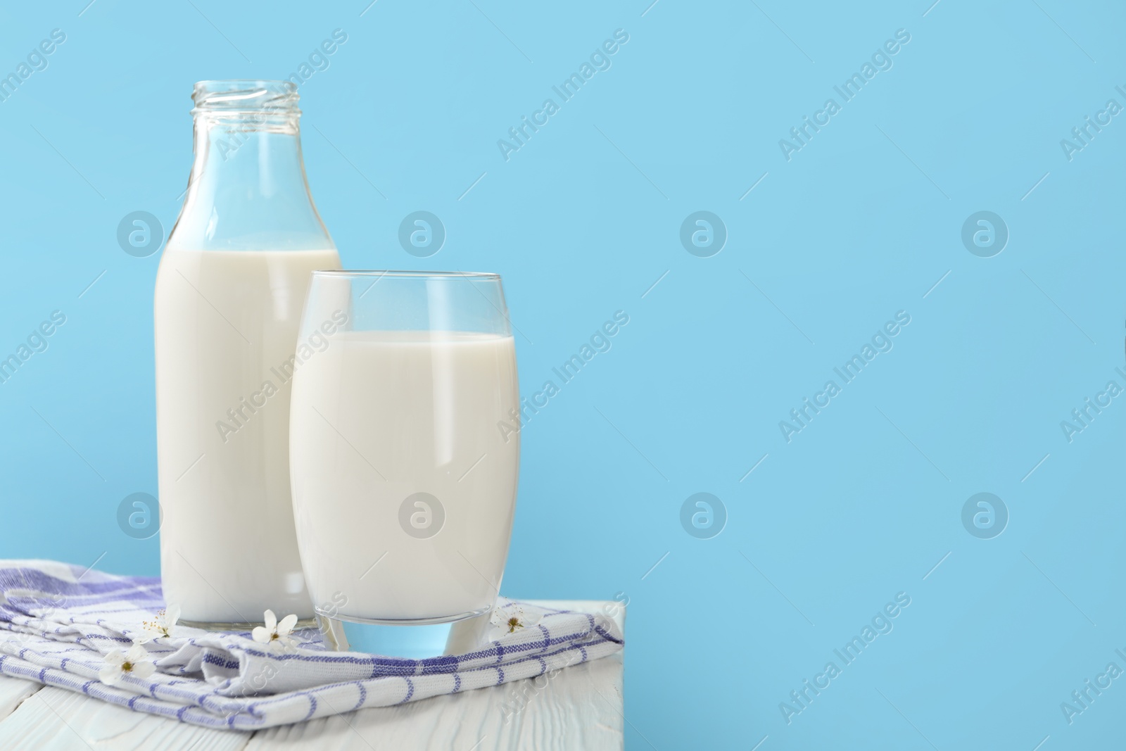 Fresh milk and blossoms on white wooden table against light blue background, closeup Photo of Fresh milk and blossoms on white wooden table against light blue background, closeup