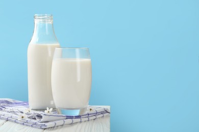 Photo of Fresh milk and blossoms on white wooden table against light blue background, closeup