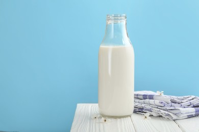 Photo of Fresh milk in bottle and blossoms on white wooden table against light blue background, closeup