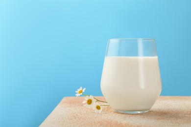 Photo of Fresh milk in glass on table against light blue background, closeup