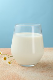 Photo of Fresh milk in glass on table against light blue background, closeup