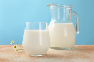 Photo of Fresh milk and flowers on table against light blue background, closeup
