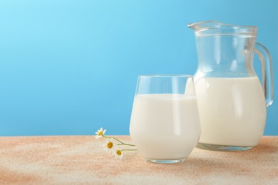 Photo of Fresh milk and flowers on table against light blue background, closeup. Space for text
