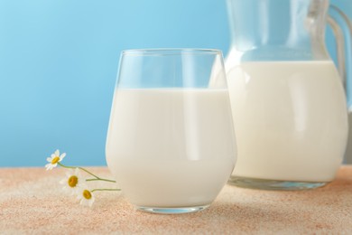 Photo of Fresh milk and flowers on table against light blue background, closeup