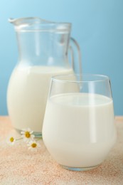 Photo of Fresh milk and flowers on table against light blue background, closeup