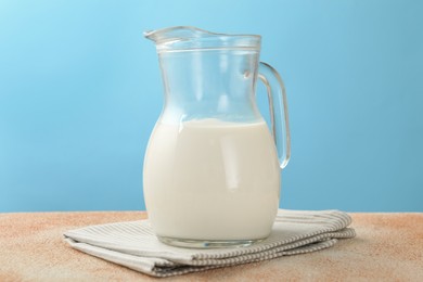 Photo of Fresh milk in jug on table against light blue background, closeup