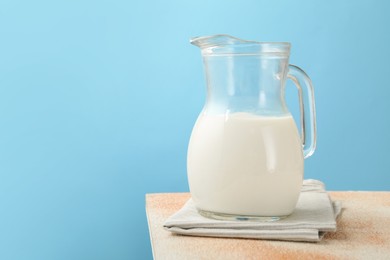 Photo of Fresh milk in jug on table against light blue background, closeup