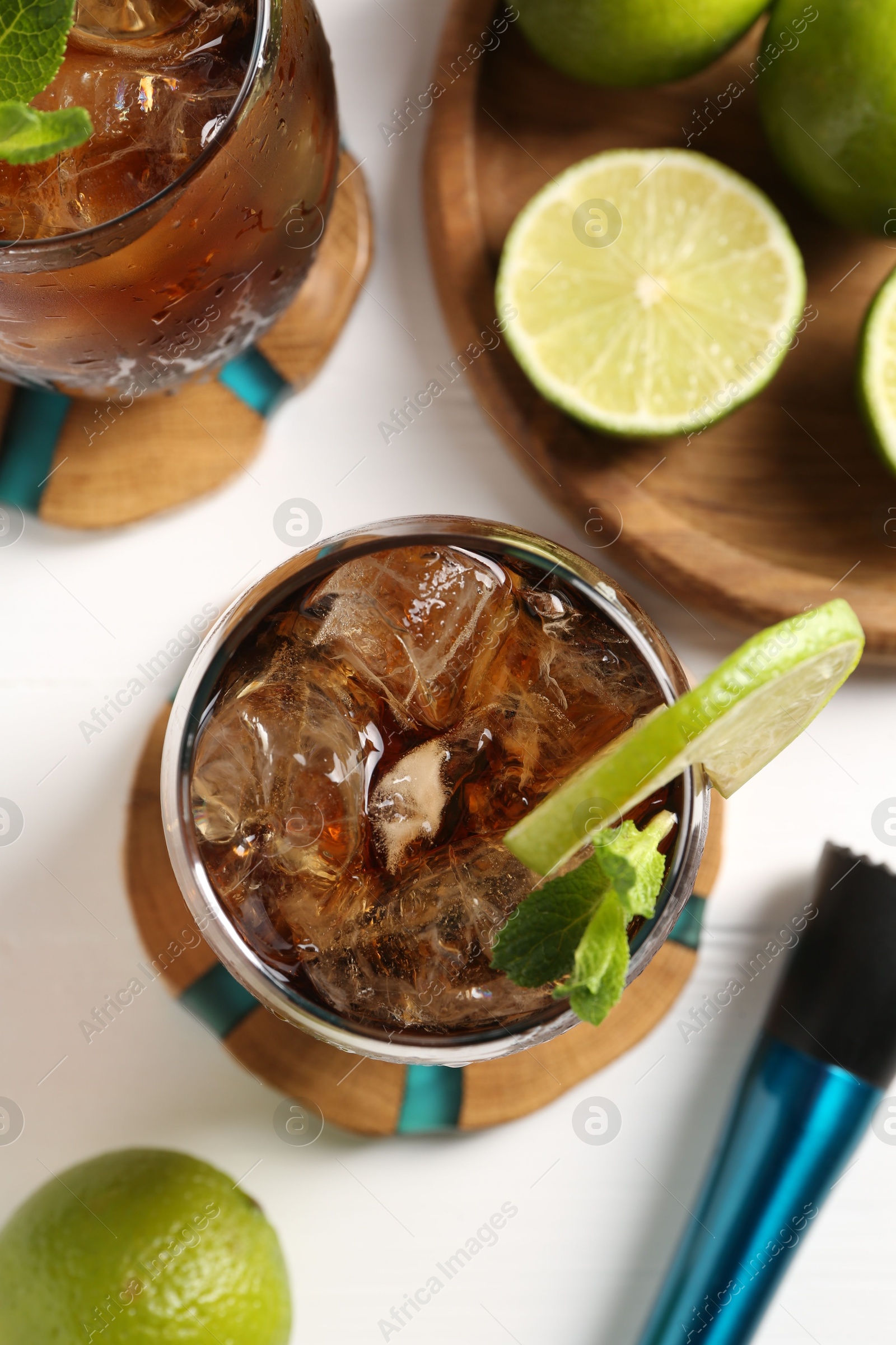 Tasty Cuba Libre cocktail in glasses, limes and muddler on white table, flat lay Photo of Tasty Cuba Libre cocktail in glasses, limes and muddler on white table, flat lay