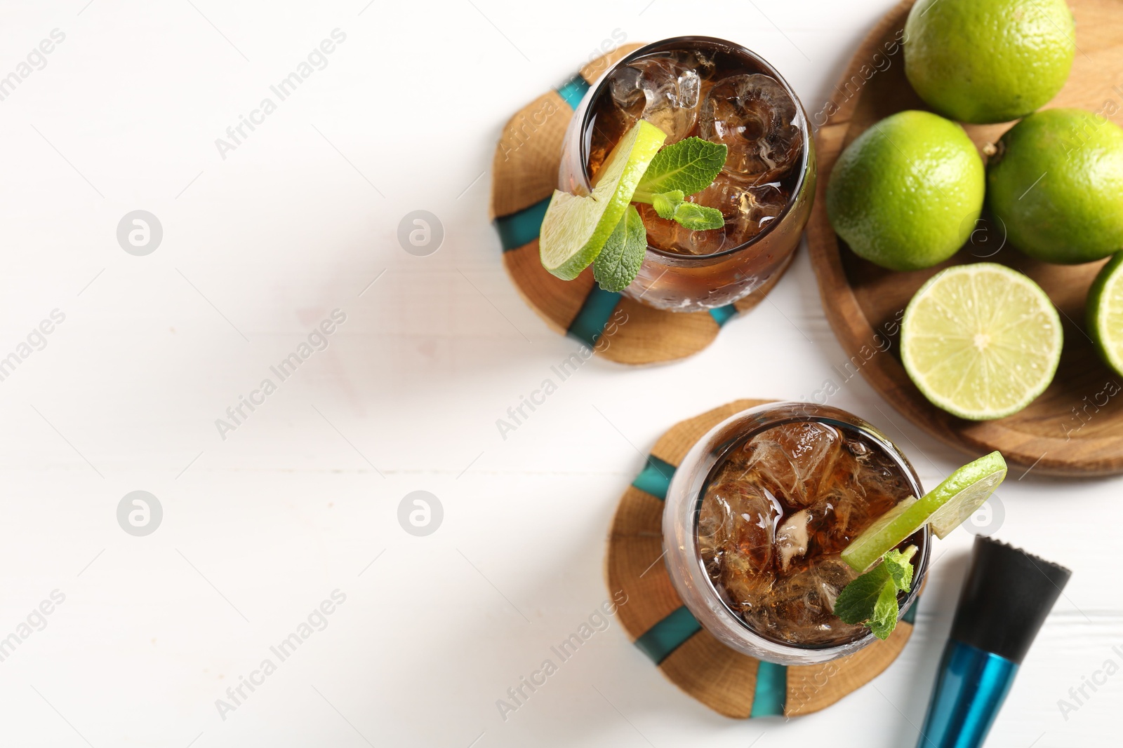 Tasty Cuba Libre cocktail in glasses, limes and muddler on white table, flat lay. Space for text Photo of Tasty Cuba Libre cocktail in glasses, limes and muddler on white table, flat lay. Space for text