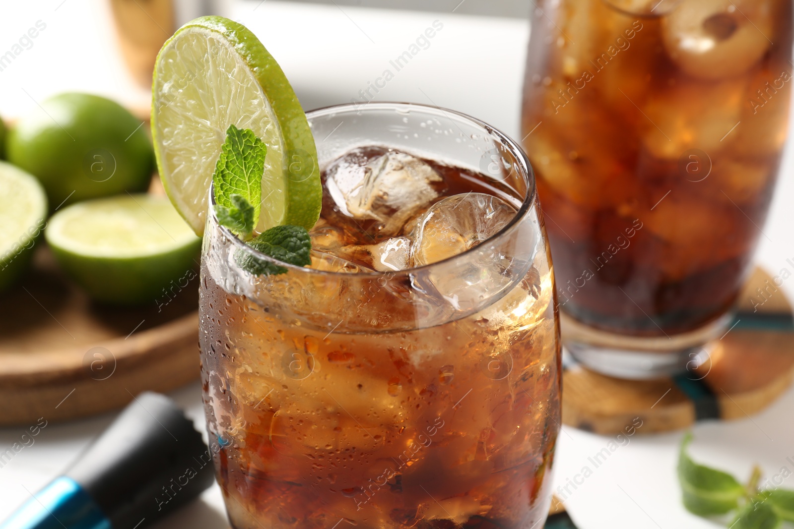 Tasty Cuba Libre cocktail in glasses, ingredients and muddler on white table, closeup Photo of Tasty Cuba Libre cocktail in glasses, ingredients and muddler on white table, closeup