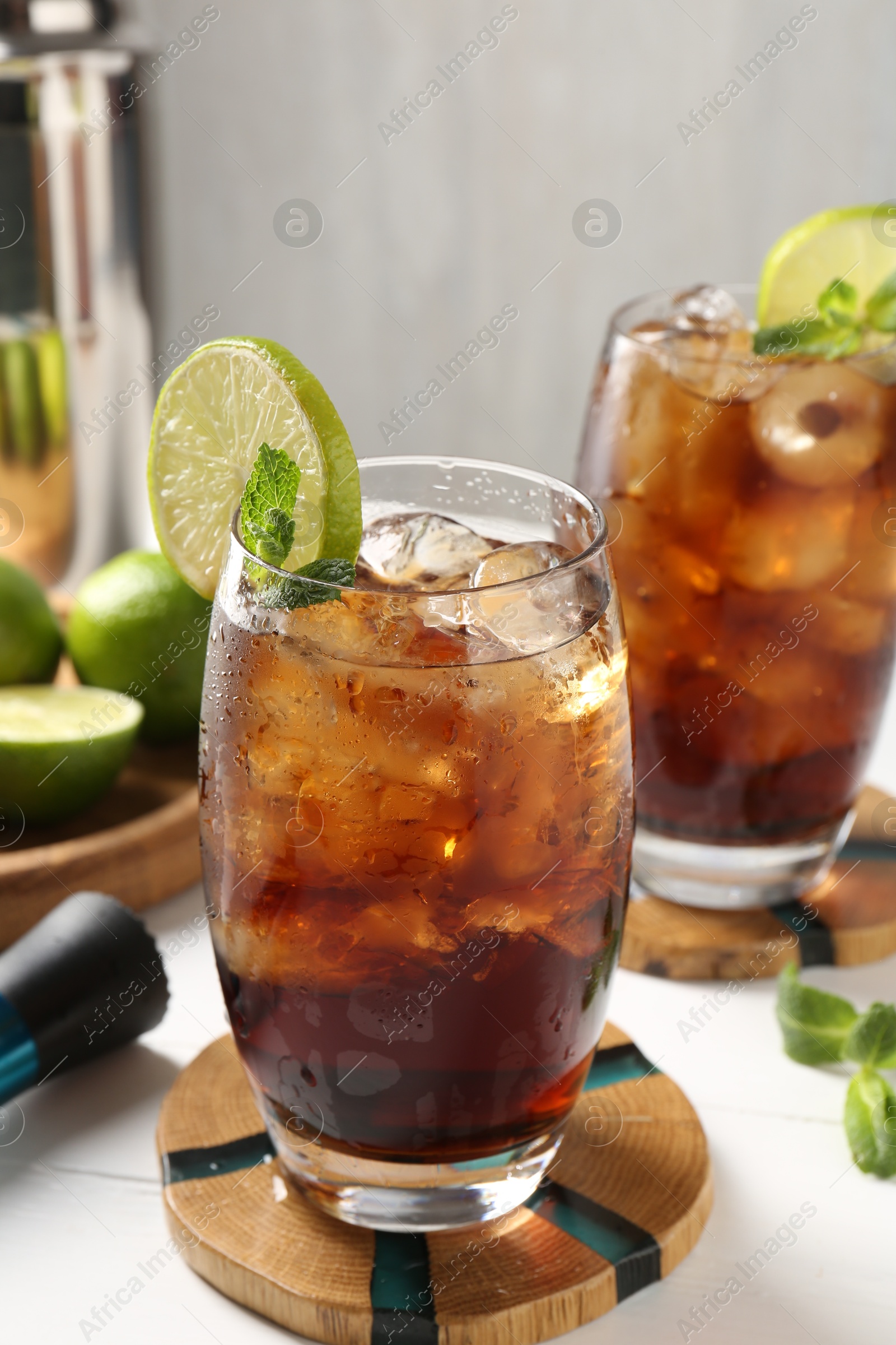 Tasty Cuba Libre cocktail in glasses, ingredients and muddler on white table, closeup Photo of Tasty Cuba Libre cocktail in glasses, ingredients and muddler on white table, closeup