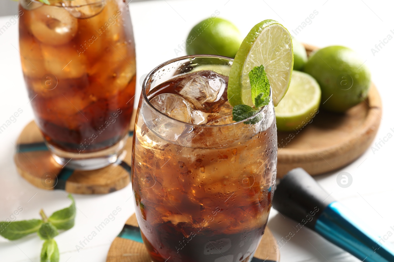 Tasty Cuba Libre cocktail in glasses, ingredients and muddler on white table, closeup Photo of Tasty Cuba Libre cocktail in glasses, ingredients and muddler on white table, closeup