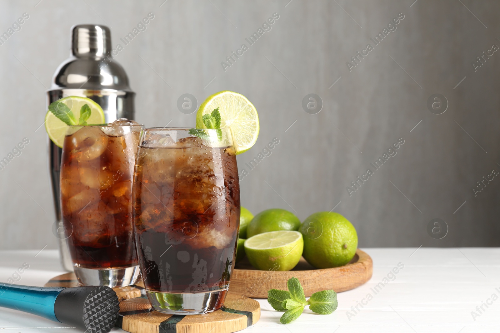 Tasty Cuba Libre cocktail in glasses, ingredients, muddler and shaker on white wooden table, space for text Photo of Tasty Cuba Libre cocktail in glasses, ingredients, muddler and shaker on white wooden table, space for text