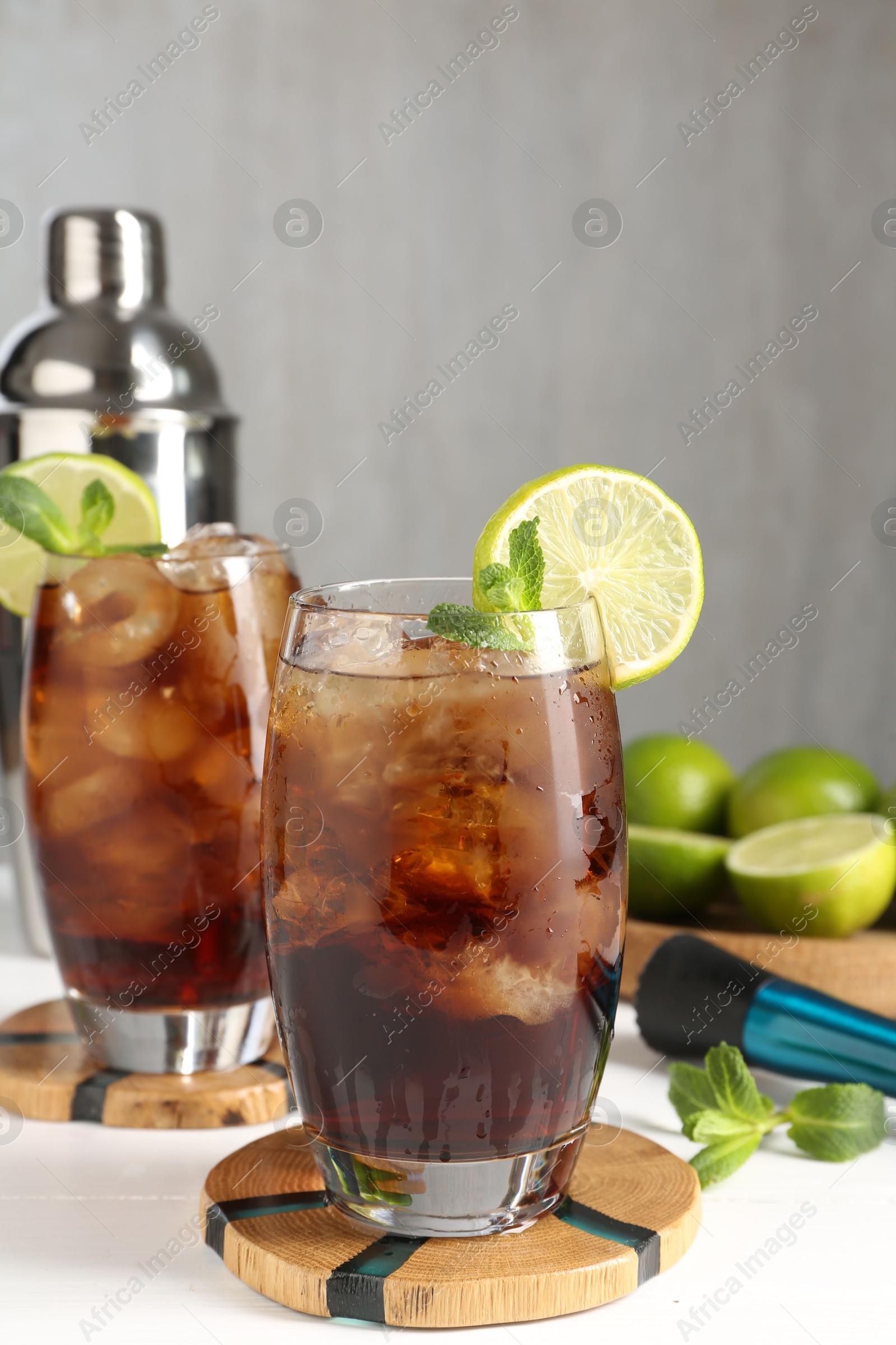 Tasty Cuba Libre cocktail in glasses, ingredients, muddler and shaker on white wooden table Photo of Tasty Cuba Libre cocktail in glasses, ingredients, muddler and shaker on white wooden table
