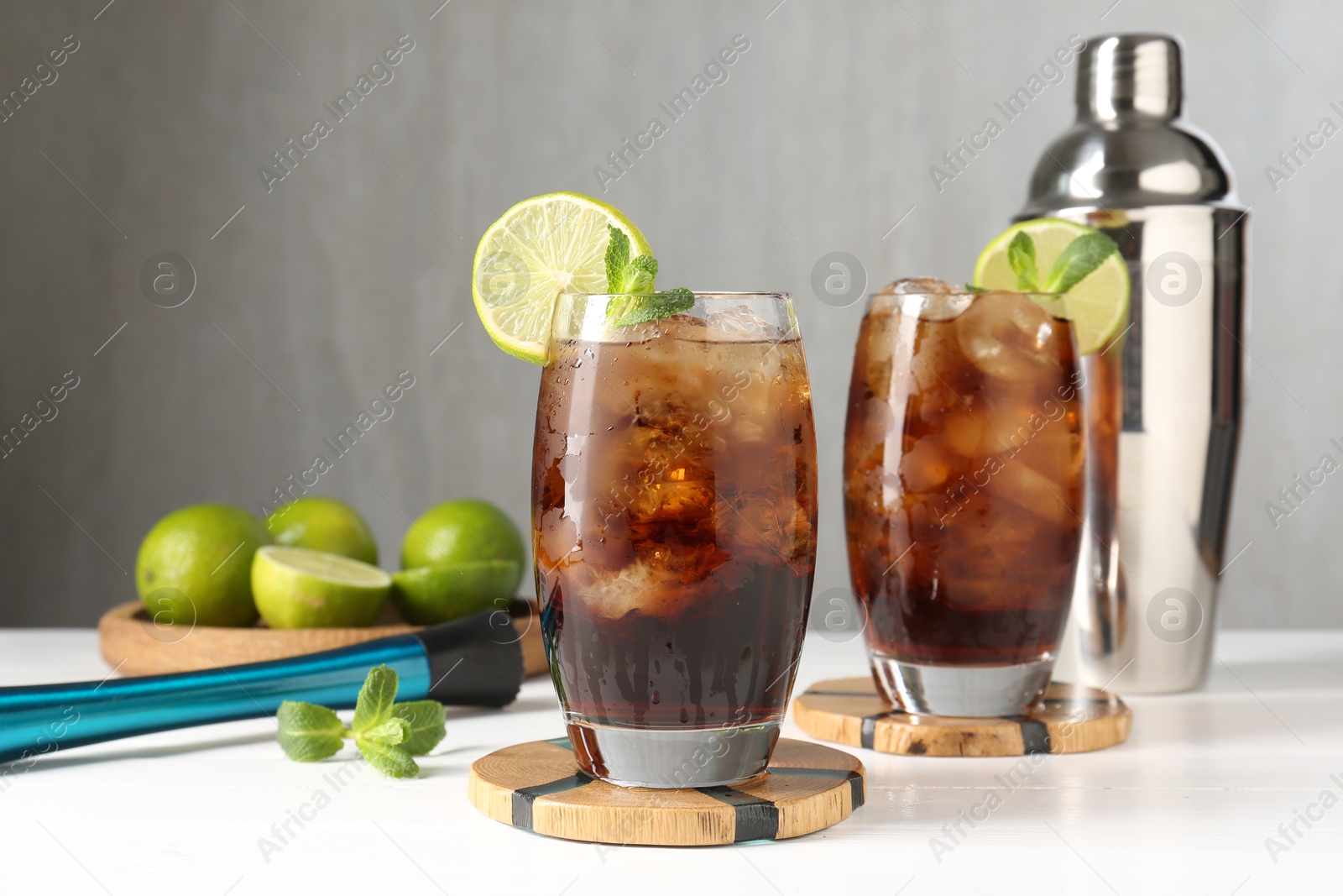 Tasty Cuba Libre cocktail in glasses, ingredients, muddler and shaker on white wooden table Photo of Tasty Cuba Libre cocktail in glasses, ingredients, muddler and shaker on white wooden table