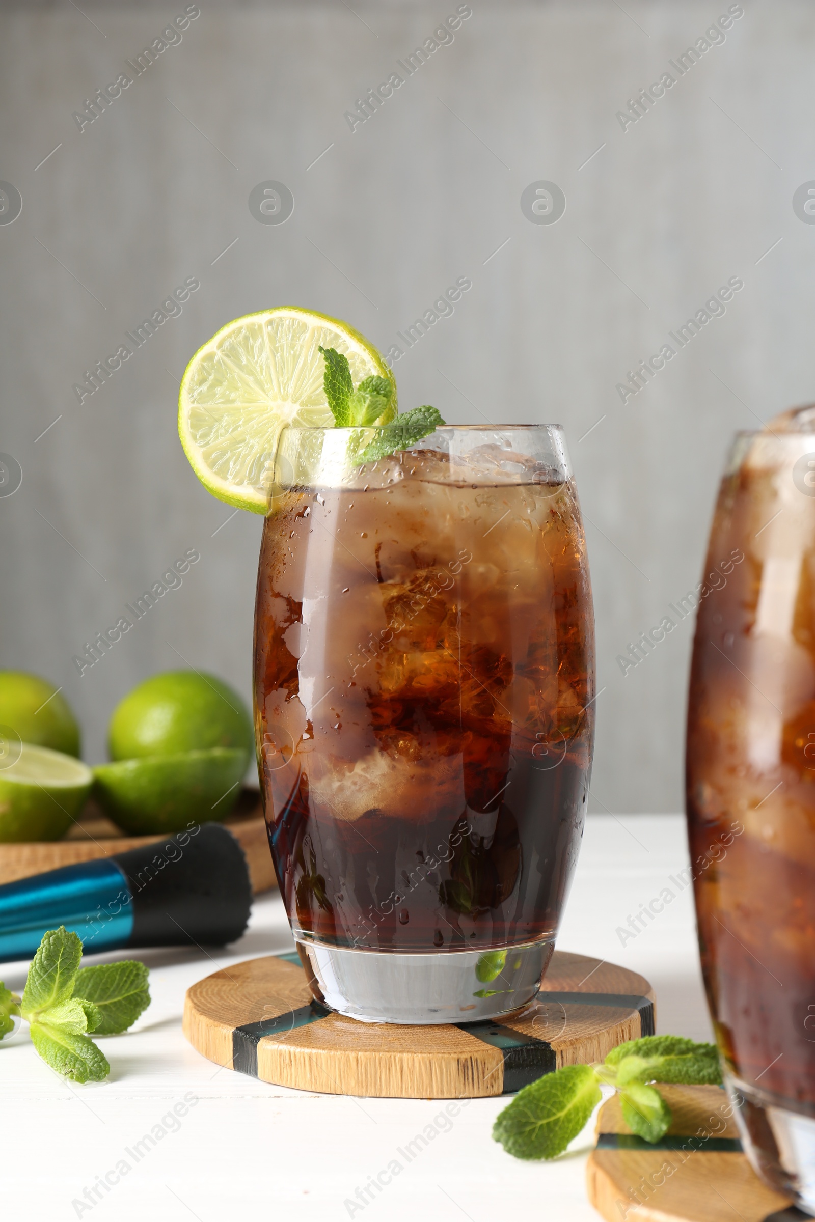 Tasty Cuba Libre cocktail in glasses, ingredients and muddler on white table Photo of Tasty Cuba Libre cocktail in glasses, ingredients and muddler on white table