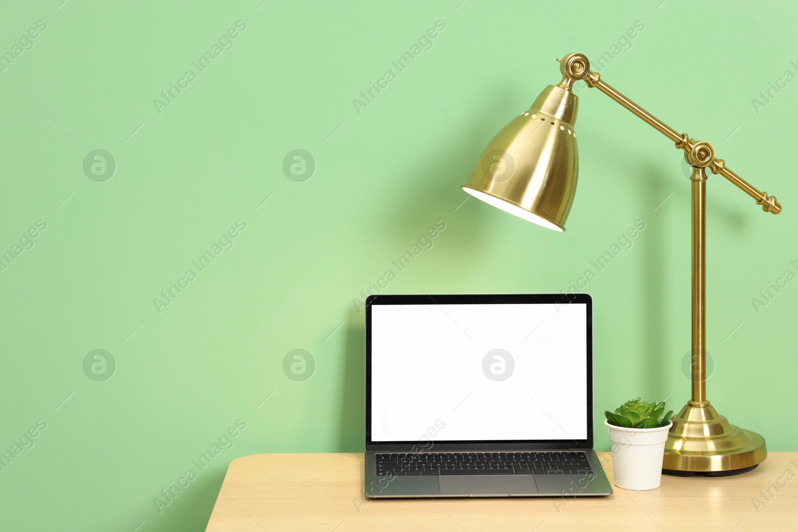 Stylish workplace with modern laptop on wooden desk near light green wall. Space for text Photo of Stylish workplace with modern laptop on wooden desk near light green wall. Space for text