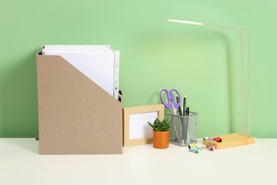 Photo of Stylish workplace with lamp, stationery and plant on white desk near light green wall