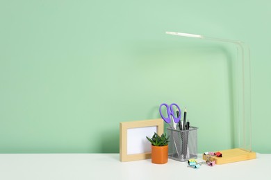 Photo of Stylish workplace with lamp, stationery and plant on white desk near light green wall. Space for text