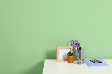 Photo of Stylish workplace with stationery and plant on white desk near light green wall. Space for text
