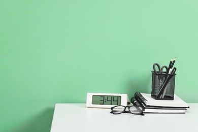 Photo of Stylish workplace with stationery and clock on white desk near light green wall. Space for text