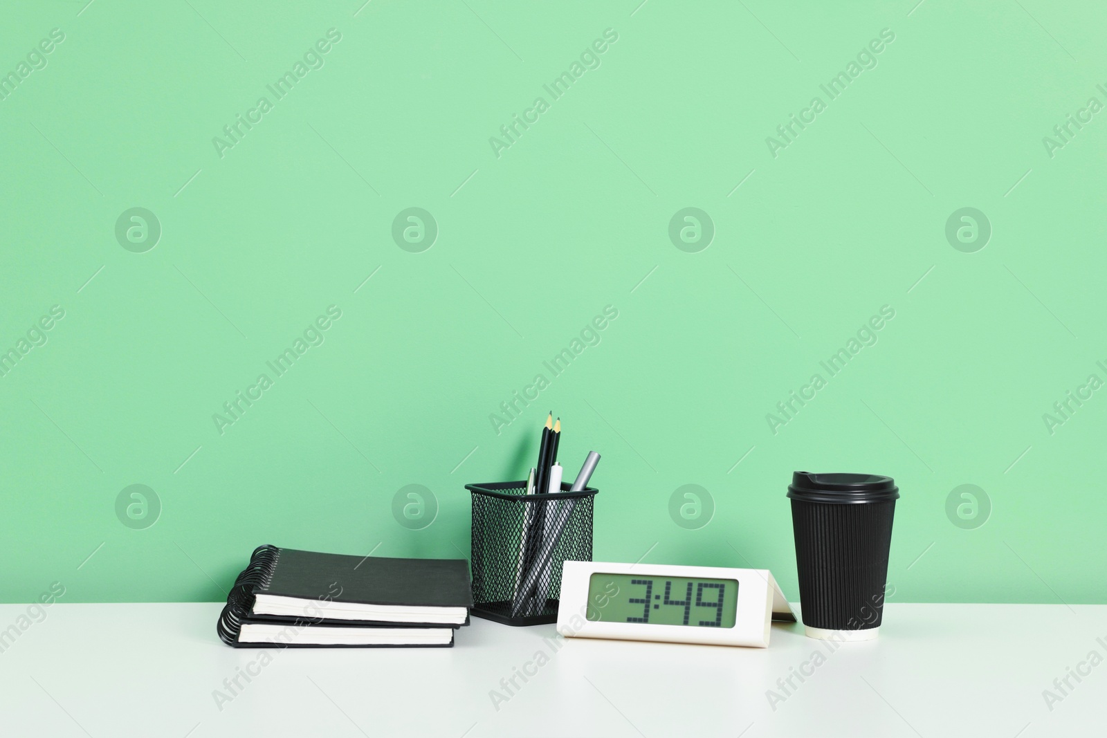 Stylish workplace with stationery and clock on white desk near light green wall. Space for text Photo of Stylish workplace with stationery and clock on white desk near light green wall. Space for text