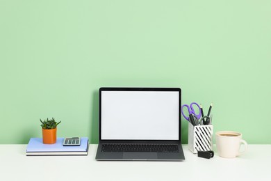 Photo of Stylish workplace with modern laptop on white desk near light green wall